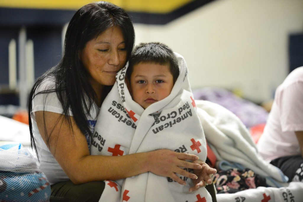 Claudia Martinez sitting on a cot with her son wrapped in a blanket. 