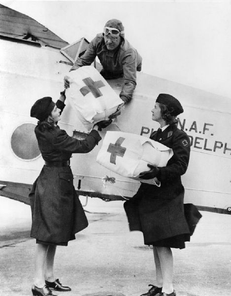 December 1941. Philadelphia, Pennsylvania. Red Cross Motor Corps members are shown above handing the test cartons of plasma to the Navy pilot who will drop them on land and water.