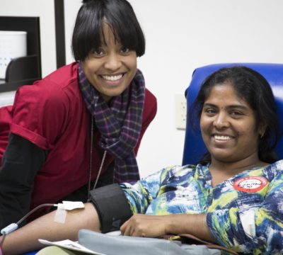 Red Cross collections staff member smiles while collecting blood from donor.