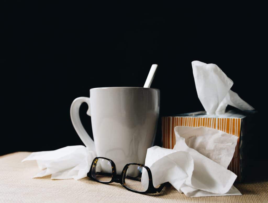 Table with a pair of glasses, facial tissues and a mug on it 