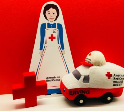 Cutout Clara standing with a Red Cross and a toy emergency response vehicle.