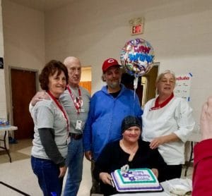 A group photo of Deborah with her cake, her husband and three Red Cross volunteers