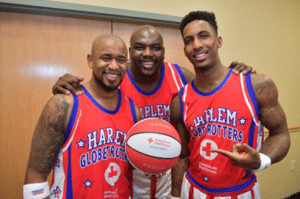 Three Harlem Globetrotters hold a Red Cross basketball in their hands. 
