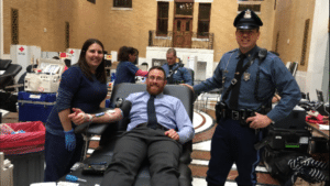 Officer Dic giving blood while Chris is standing next to him. 