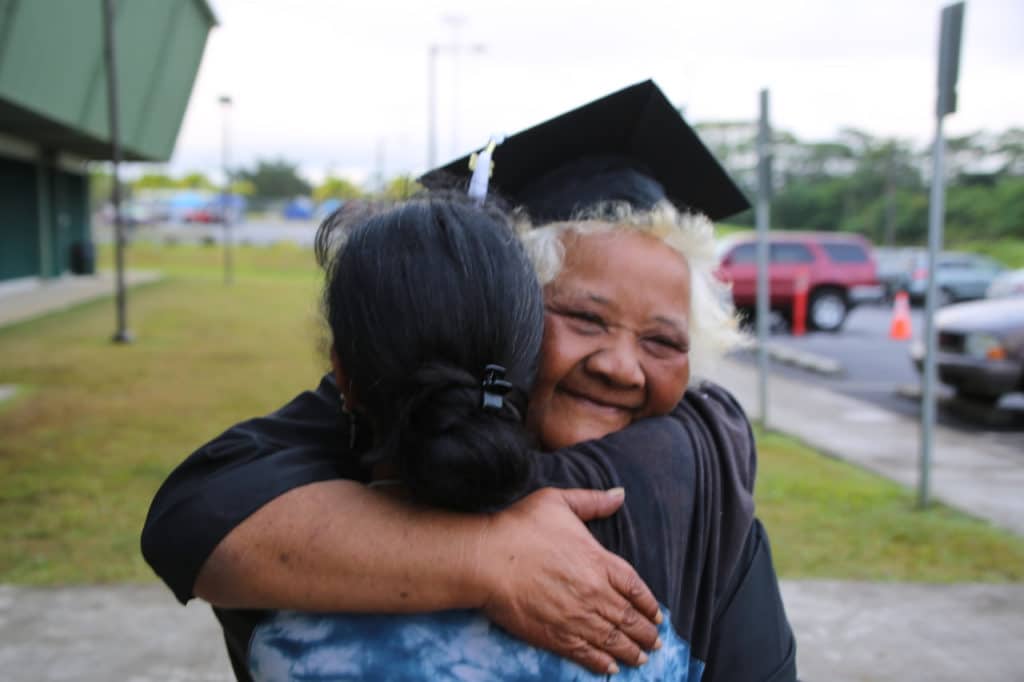 Woman wearing graduation cap hugging someone
