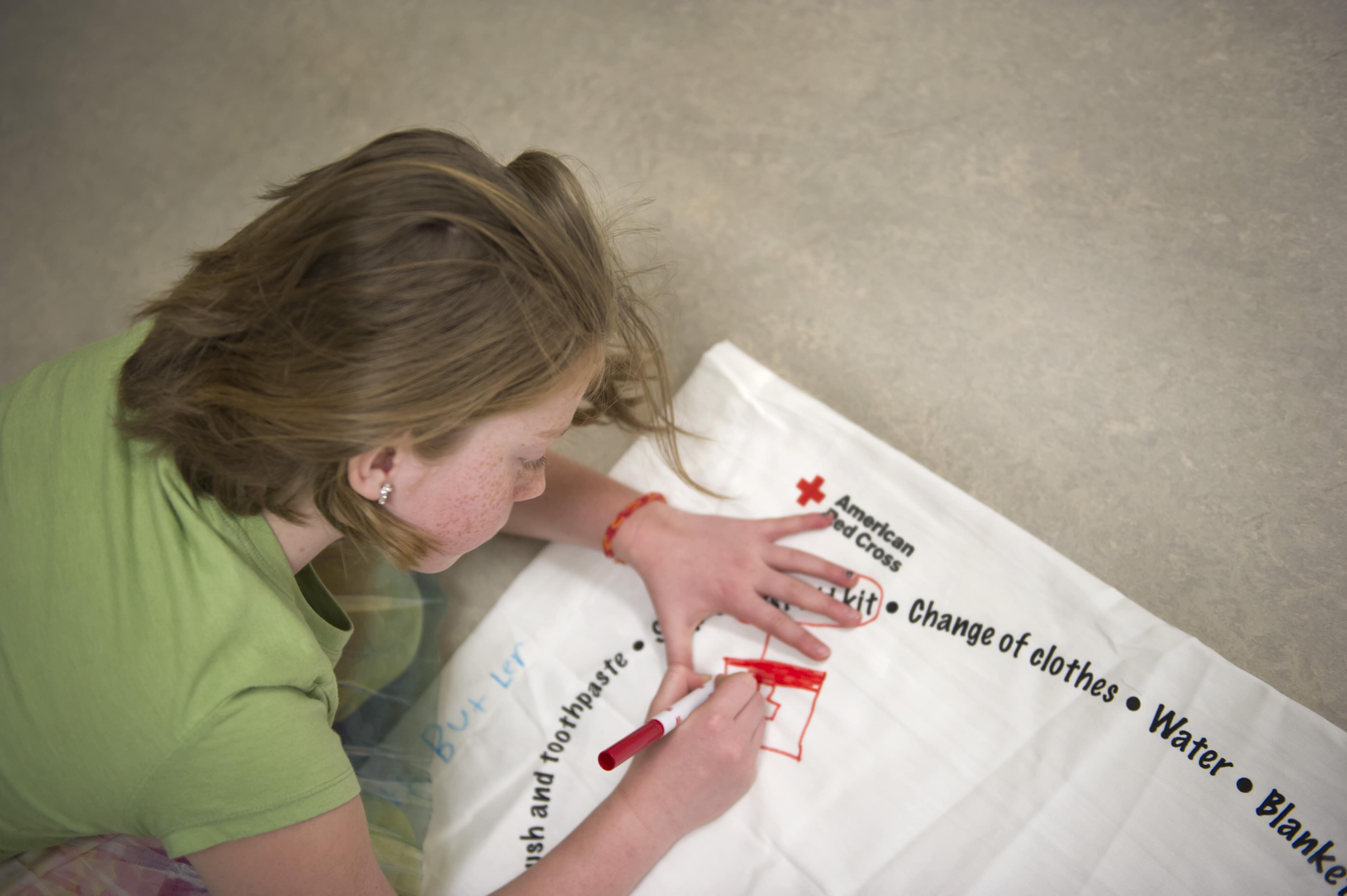 A student personalizes her pillowcase given by the Red Cross to store her emergency supplies in preparation for future weather emergencies during the Pillowcase Project event at her school. 