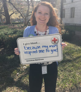 Katie holding up a sign that says "I give blood because my mom inspired me to give!"