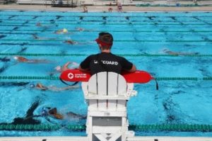 Lifeguard sitting in a chair looking over a pool at an aquatic facility.