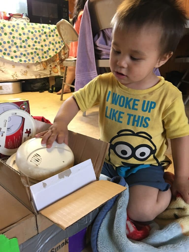 A little boy digging through a box of smoke alarms in his house.