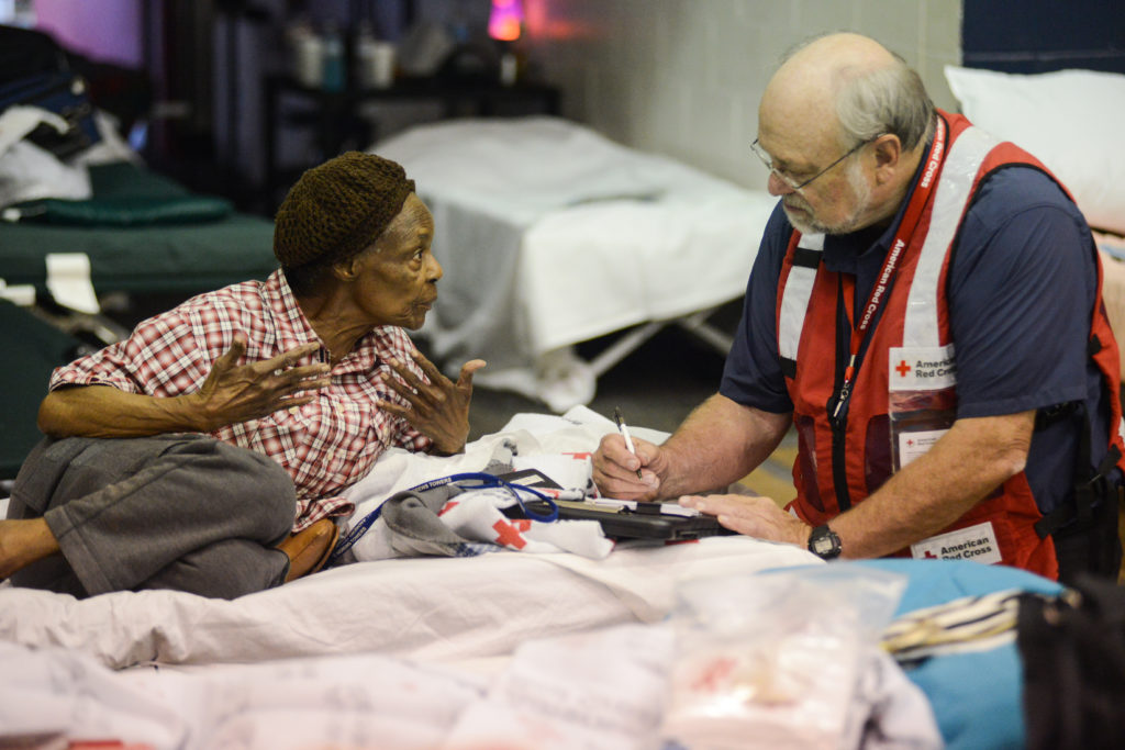 An elderly woman laying on a cot talking to a Red Cross volunteer. 