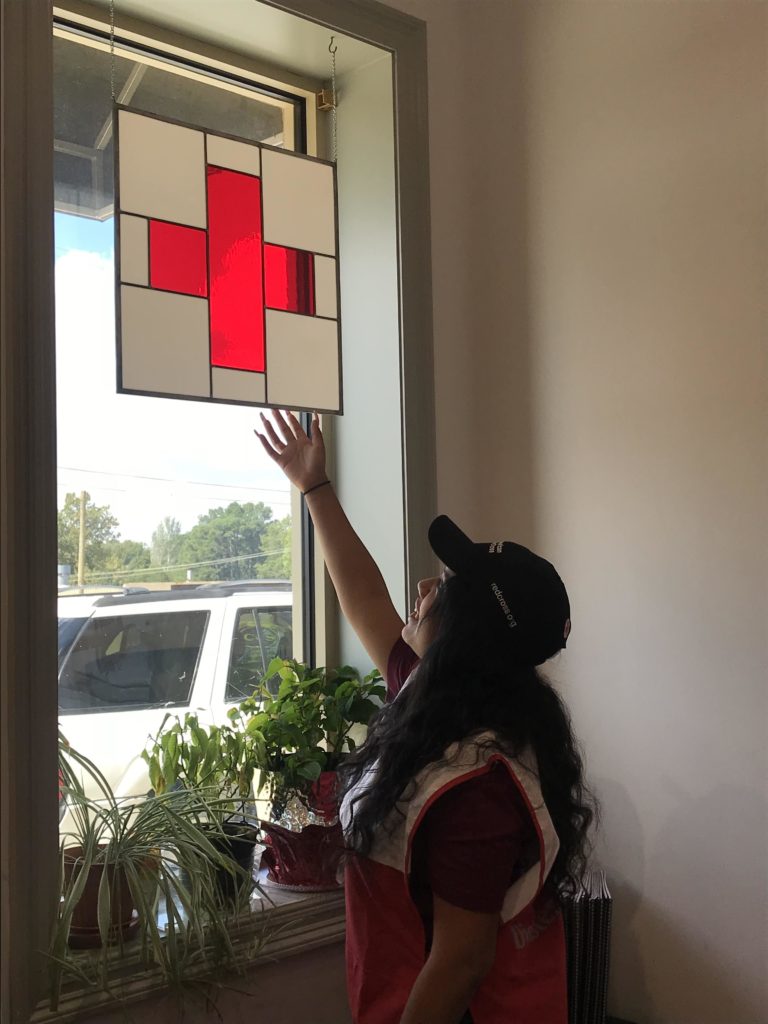 Mariana pointing toward the Red Cross emblem on the window at her office. 