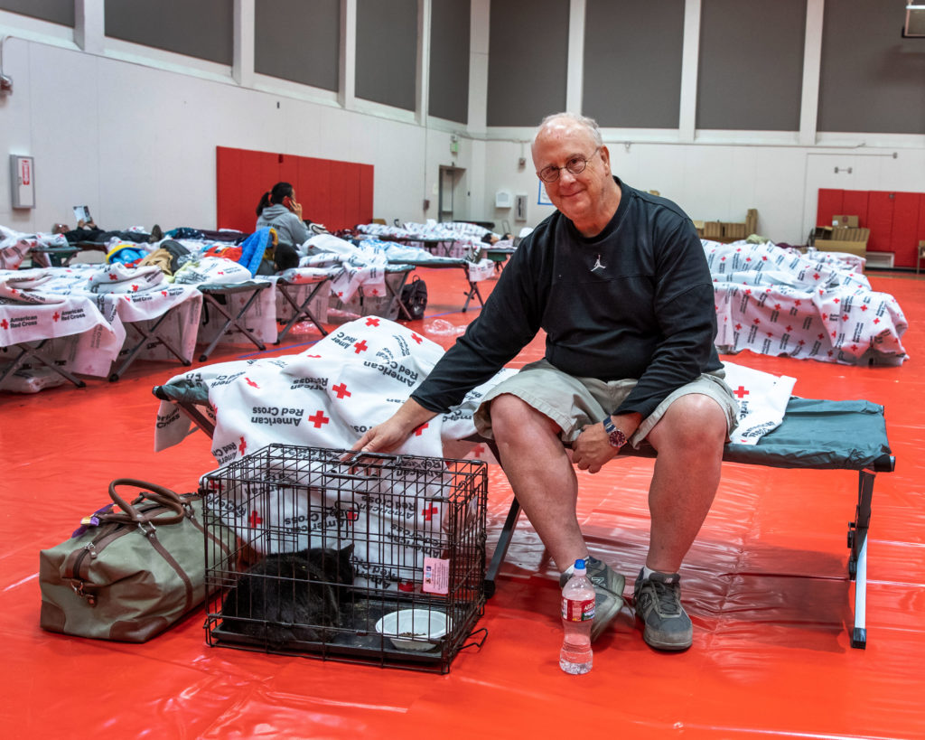 A Red Cross shelter resident sitting on a cot next to his pet cat.