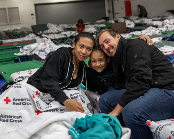 A family smiling together on a cot in a Red Cross shelter. 