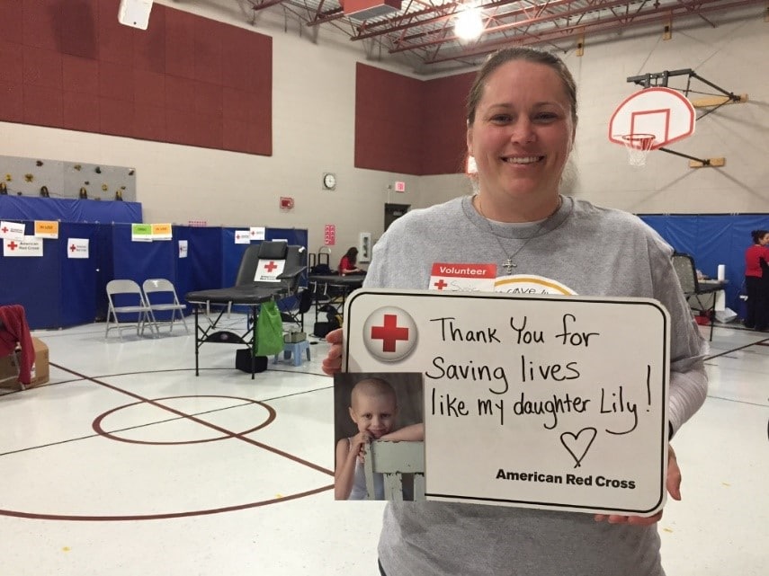 Lily's mom holding up a sign that thanks blood donors for saving her daughter's life. 