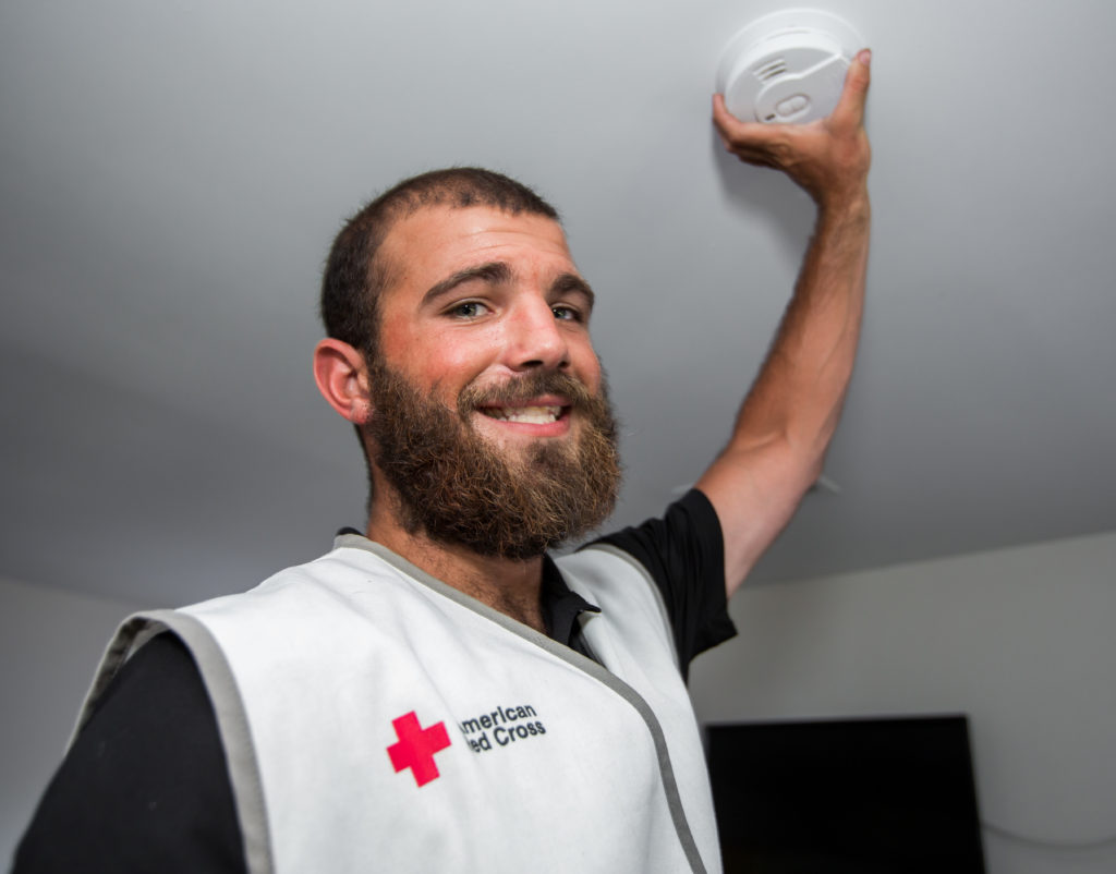 a Red Cross volunteer smiling and installing a smoke alarm. 