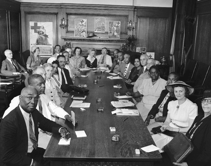 A historical photo of Mary McLeod Bethune sitting at a table during a Red Cross committee meeting.