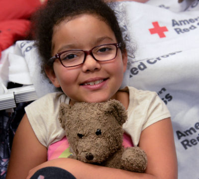 A little girl in a Red Cross shelter hugging her teddy bear.
