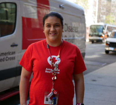 Jessenia, Red Cross home fire volunteer, standing in front of a Red Cross emergency response vehicle.