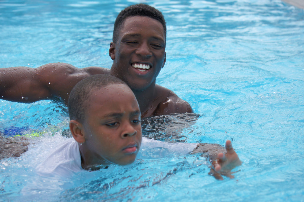 A swim instructor helping a young boy at the pool. 