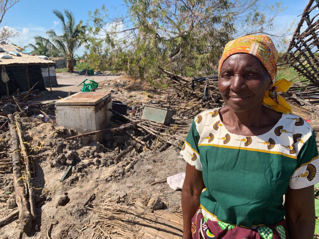 Celeste, the matriarch of her town, stands smiling in front of a pile of rubble. 