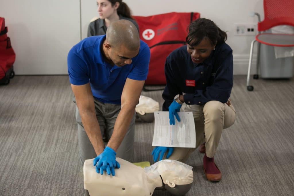 An instructor teaching CPR. The trainee is practicing compressions on a manikin. 