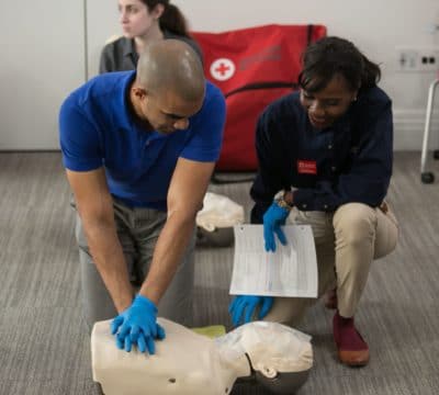 An instructor teaching CPR. The trainee is practicing compressions on a manikin.