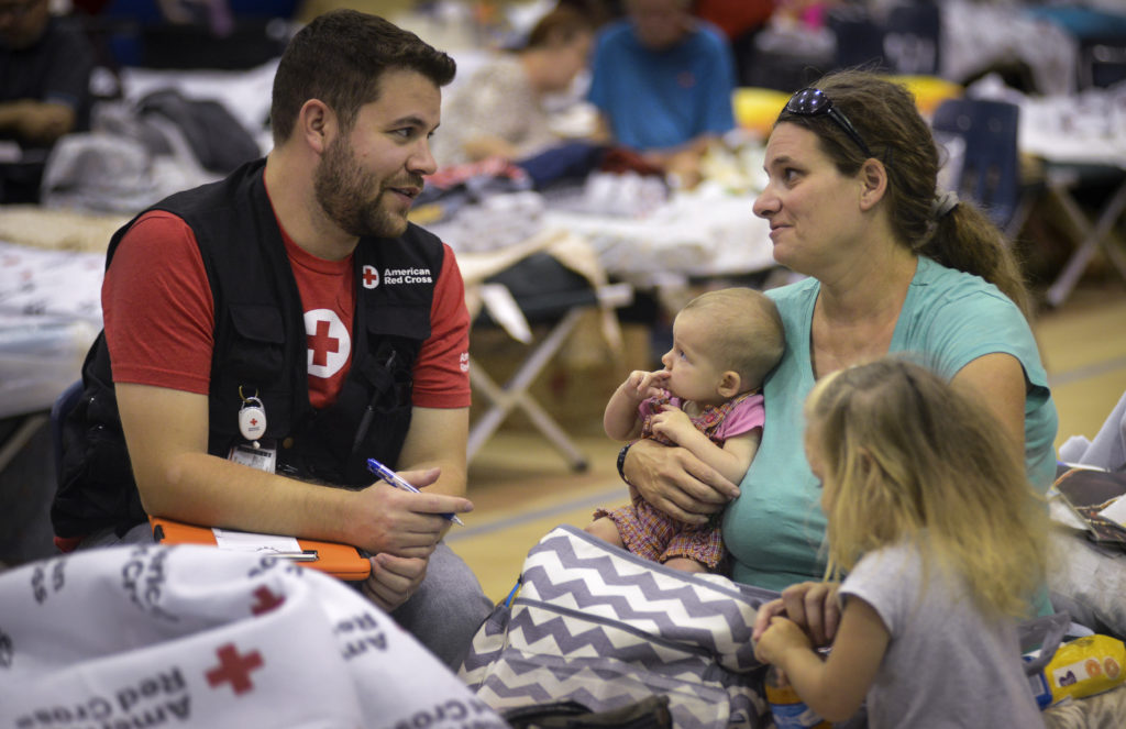 A red cross volunteer sitting with a shelter resident and her family. 