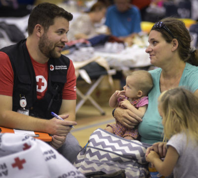 A red cross volunteer sitting with a shelter resident and her family.